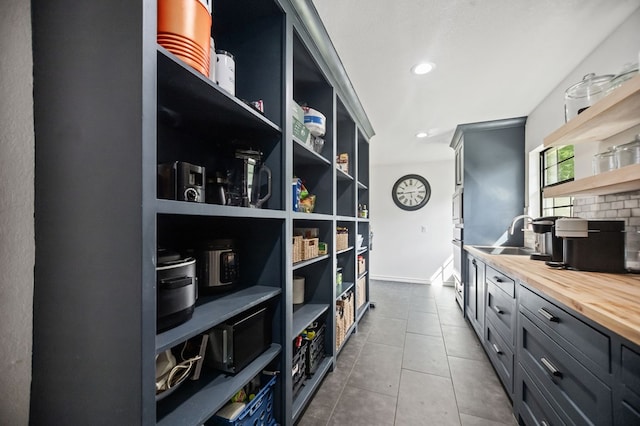 interior space with open shelves, butcher block counters, baseboards, dark tile patterned flooring, and a sink