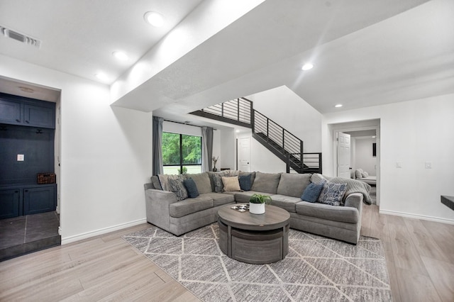 living room featuring stairs, baseboards, visible vents, and light wood-style floors