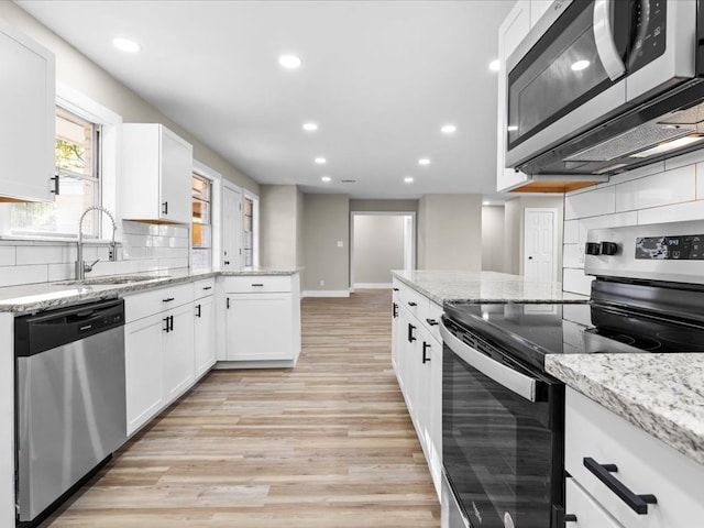 kitchen with white cabinets, decorative backsplash, light hardwood / wood-style floors, and stainless steel appliances