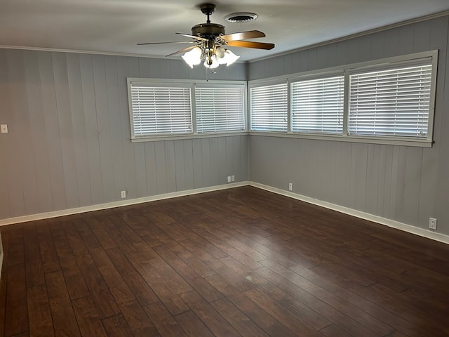 empty room featuring baseboards, visible vents, a ceiling fan, dark wood-style floors, and ornamental molding