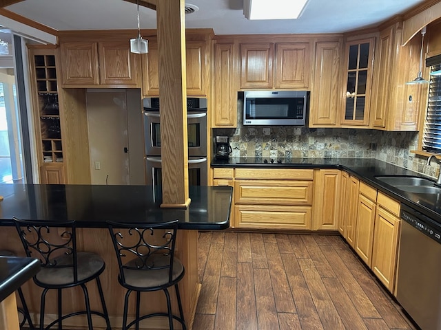 kitchen with dark countertops, appliances with stainless steel finishes, glass insert cabinets, dark wood-type flooring, and a sink