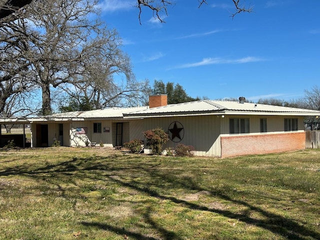 back of house with brick siding, a chimney, metal roof, and a yard