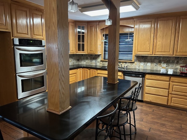 kitchen featuring dark wood-style flooring, dark countertops, backsplash, appliances with stainless steel finishes, and glass insert cabinets