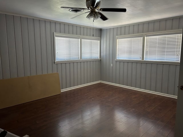 spare room with dark wood-style floors, visible vents, a ceiling fan, and baseboards