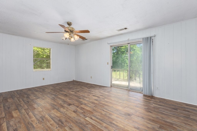empty room featuring wooden walls, visible vents, a ceiling fan, and wood finished floors