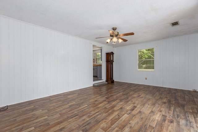 unfurnished room featuring a textured ceiling, a ceiling fan, visible vents, wood finished floors, and wooden walls