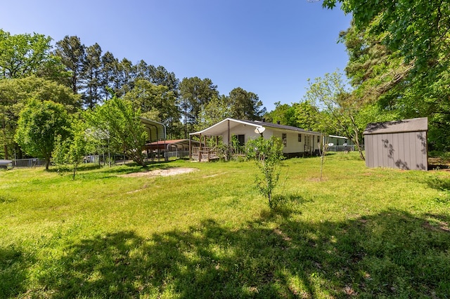 view of yard with a shed, a detached carport, fence, and an outbuilding