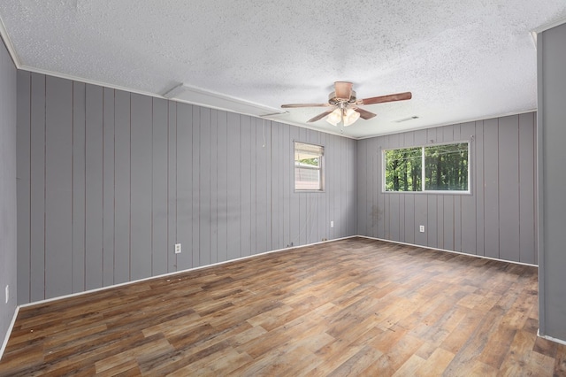unfurnished room featuring visible vents, ceiling fan, a textured ceiling, wooden walls, and wood finished floors