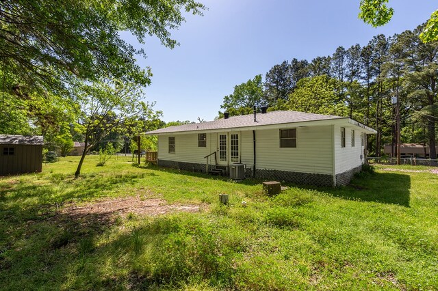 rear view of property featuring central AC unit, entry steps, a lawn, fence, and an outbuilding