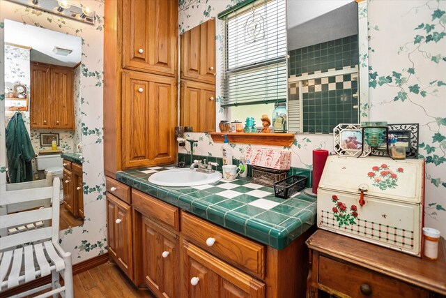 183 Holly Cir, Etoile, TX 75944 - kitchen featuring tile counters, wood finished floors, wallpapered walls, brown cabinetry, and a sink