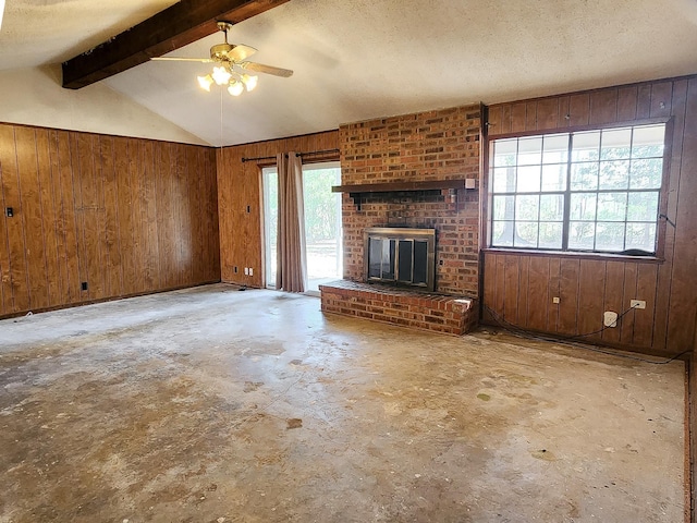 unfurnished living room with ceiling fan, lofted ceiling with beams, a textured ceiling, wooden walls, and a fireplace