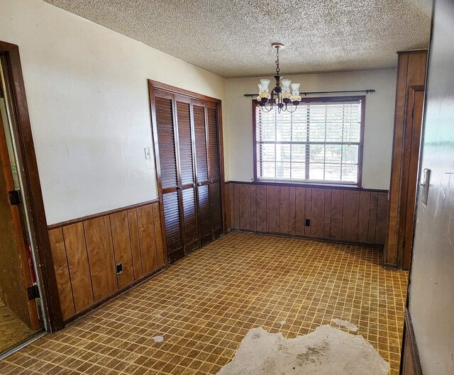 unfurnished dining area featuring a textured ceiling, wooden walls, and a notable chandelier