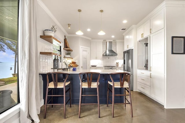 kitchen featuring wall chimney exhaust hood, hanging light fixtures, stainless steel appliances, backsplash, and white cabinets