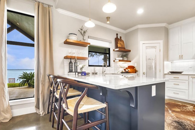 kitchen with light stone countertops, tasteful backsplash, a kitchen breakfast bar, a water view, and white cabinets