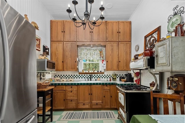 kitchen with decorative backsplash, stainless steel appliances, sink, tile countertops, and a notable chandelier