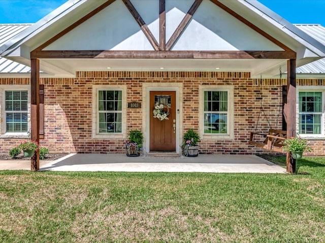 property entrance featuring metal roof, a patio, a yard, and brick siding