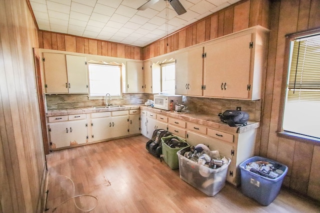 kitchen featuring white microwave, backsplash, ceiling fan, wood walls, and light wood-style floors