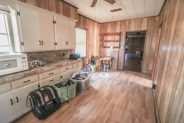 kitchen featuring ceiling fan, tile countertops, wooden walls, white cabinetry, and light hardwood / wood-style flooring