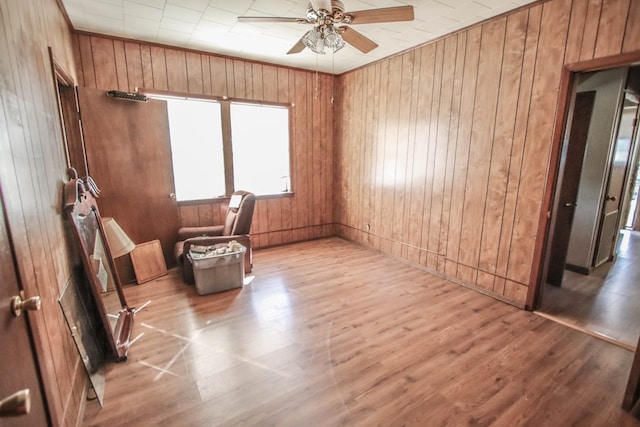 spare room featuring ceiling fan, light hardwood / wood-style flooring, and wood walls