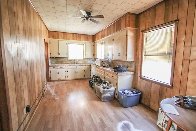 kitchen featuring ceiling fan, sink, wooden walls, and light hardwood / wood-style floors