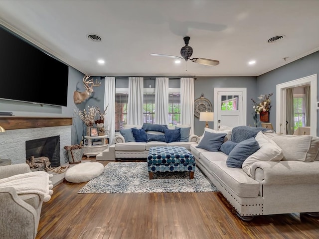 living area featuring wood finished floors, ceiling fan, a stone fireplace, and visible vents