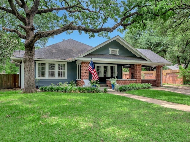 view of front facade featuring fence, a shingled roof, a front lawn, brick siding, and a porch