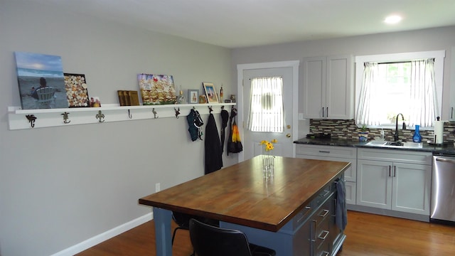 kitchen featuring stainless steel dishwasher, sink, white cabinets, a kitchen island, and butcher block counters