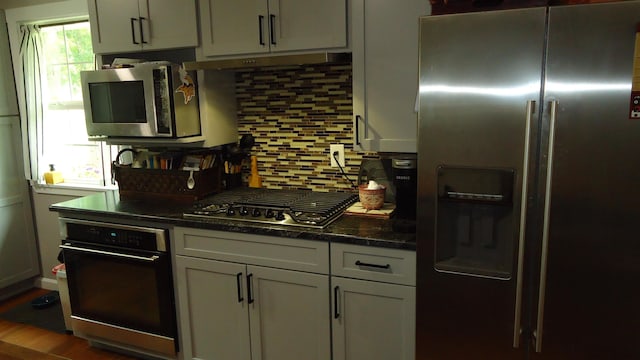 kitchen with hardwood / wood-style floors, backsplash, appliances with stainless steel finishes, and dark stone counters