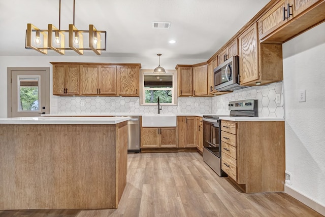 kitchen featuring appliances with stainless steel finishes, decorative light fixtures, light hardwood / wood-style flooring, and sink