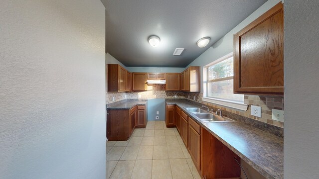 kitchen featuring decorative backsplash, sink, light tile patterned floors, and a textured ceiling