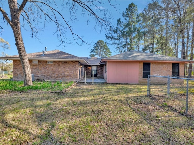 rear view of house with a lawn, fence, and stone siding
