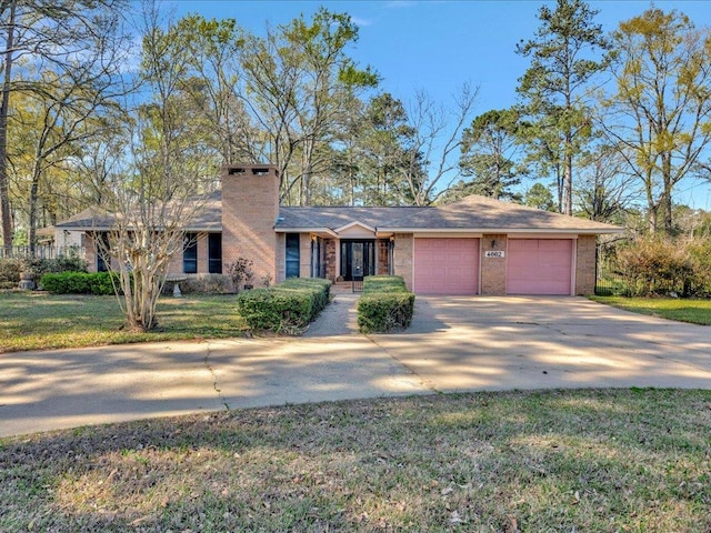 view of front of house with a front lawn, brick siding, driveway, a chimney, and an attached garage