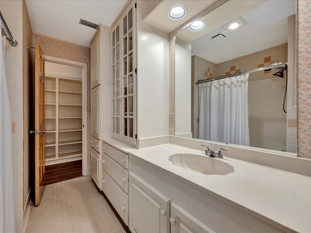 bathroom with vanity, curtained shower, a walk in closet, visible vents, and tile patterned flooring