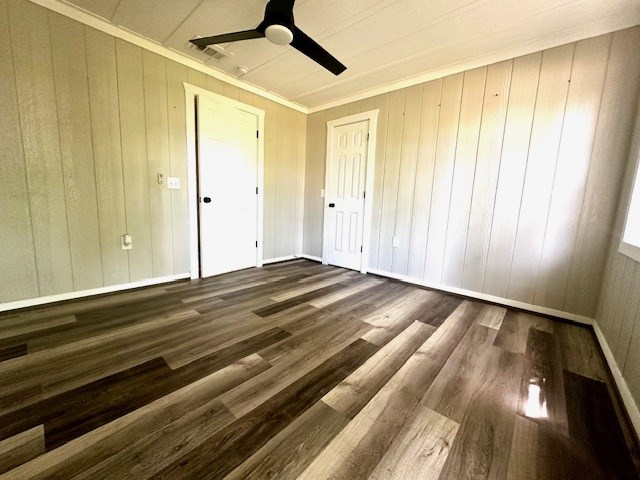 unfurnished bedroom with wood walls, a ceiling fan, dark wood-type flooring, visible vents, and ornamental molding