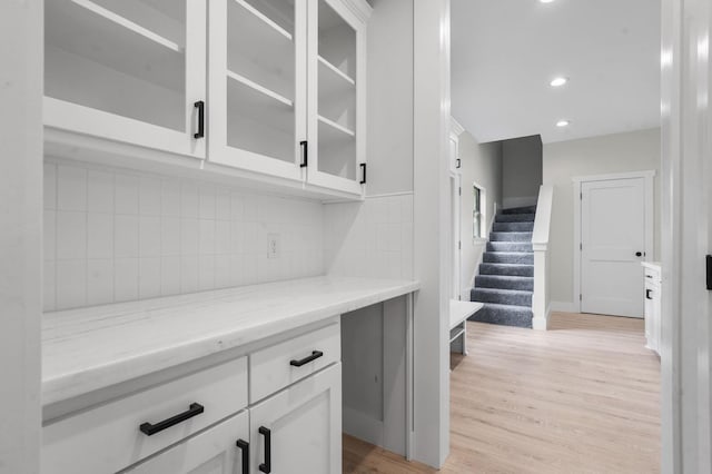 bar with white cabinets, decorative backsplash, light stone countertops, and light wood-type flooring