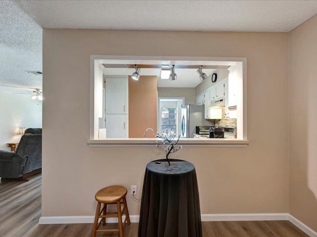 kitchen featuring white cabinets, a kitchen breakfast bar, hardwood / wood-style flooring, a textured ceiling, and kitchen peninsula