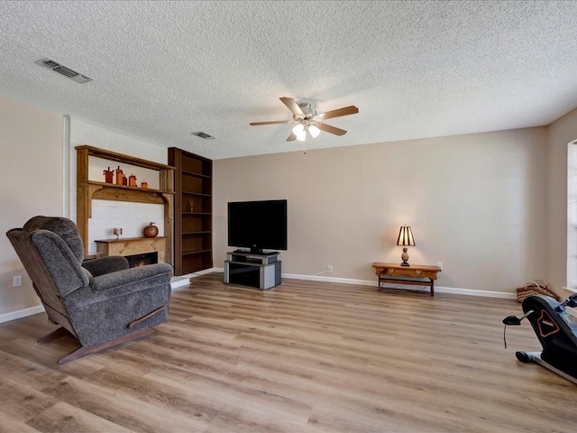 living room featuring ceiling fan, light hardwood / wood-style floors, and a textured ceiling