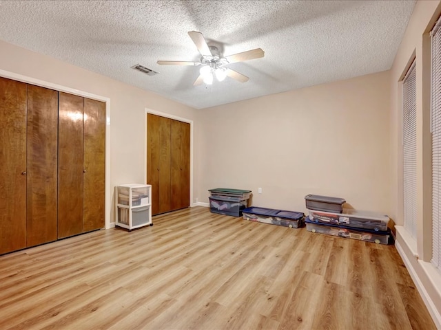 bedroom featuring a textured ceiling, light hardwood / wood-style floors, ceiling fan, and multiple closets