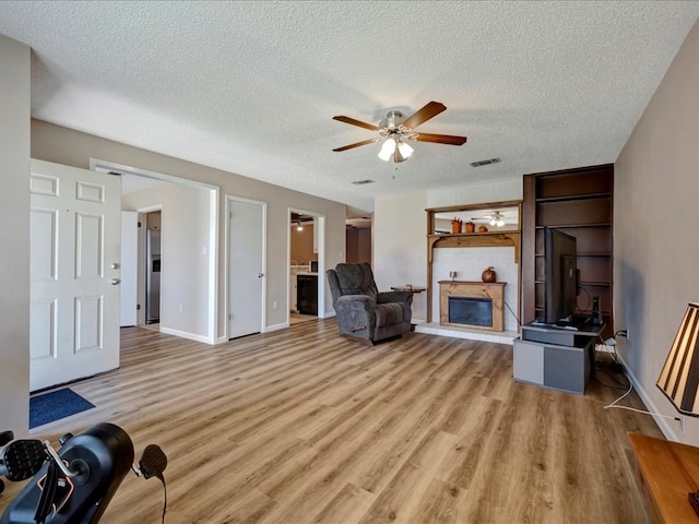 living room featuring ceiling fan, light hardwood / wood-style flooring, and a textured ceiling