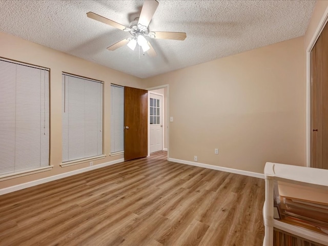 unfurnished bedroom with ceiling fan, light hardwood / wood-style floors, a textured ceiling, and multiple closets