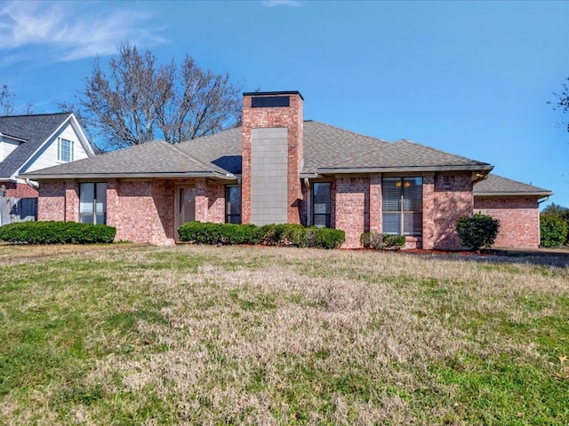 view of front of home featuring brick siding, a shingled roof, a chimney, and a front yard