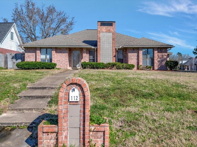 view of front of home featuring a shingled roof, brick siding, a chimney, and a front lawn