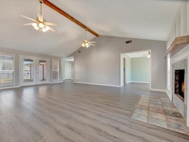 unfurnished living room with beam ceiling, french doors, light wood finished floors, visible vents, and a tile fireplace