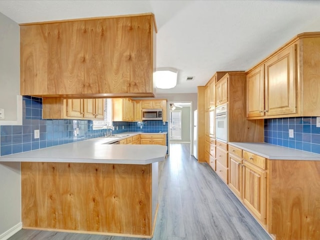 kitchen with stainless steel microwave, white oven, a peninsula, light countertops, and light brown cabinets