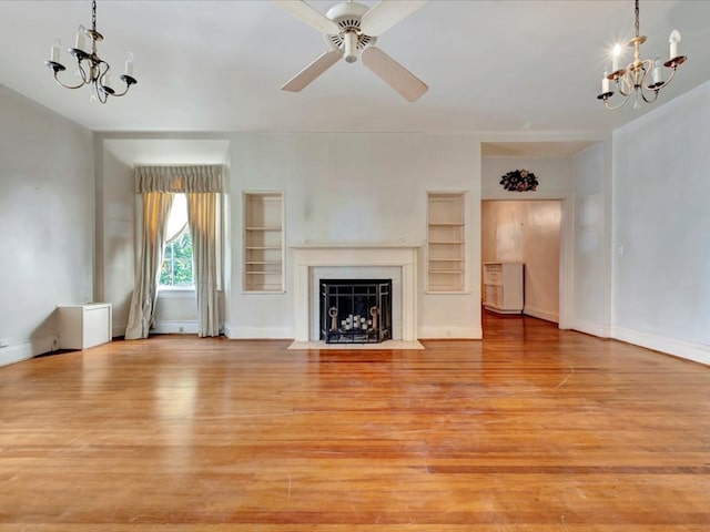 unfurnished living room with ceiling fan with notable chandelier, built in shelves, and light wood-type flooring