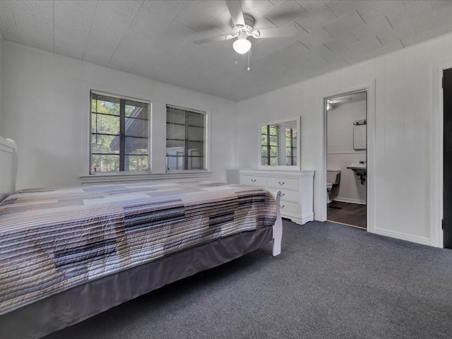 bedroom featuring ensuite bathroom, dark carpet, multiple windows, and ceiling fan