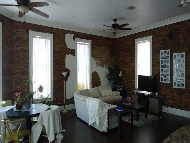 living room with ceiling fan, dark wood-type flooring, brick wall, and ornamental molding