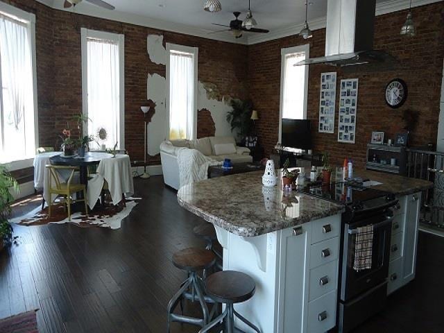 kitchen with black / electric stove, white cabinetry, a wealth of natural light, and brick wall