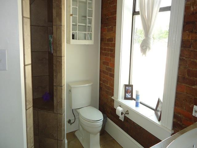 bathroom with tile patterned flooring, toilet, and brick wall