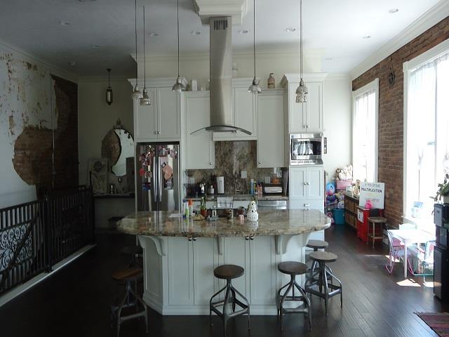 kitchen with pendant lighting, a center island with sink, island range hood, light stone counters, and stainless steel appliances